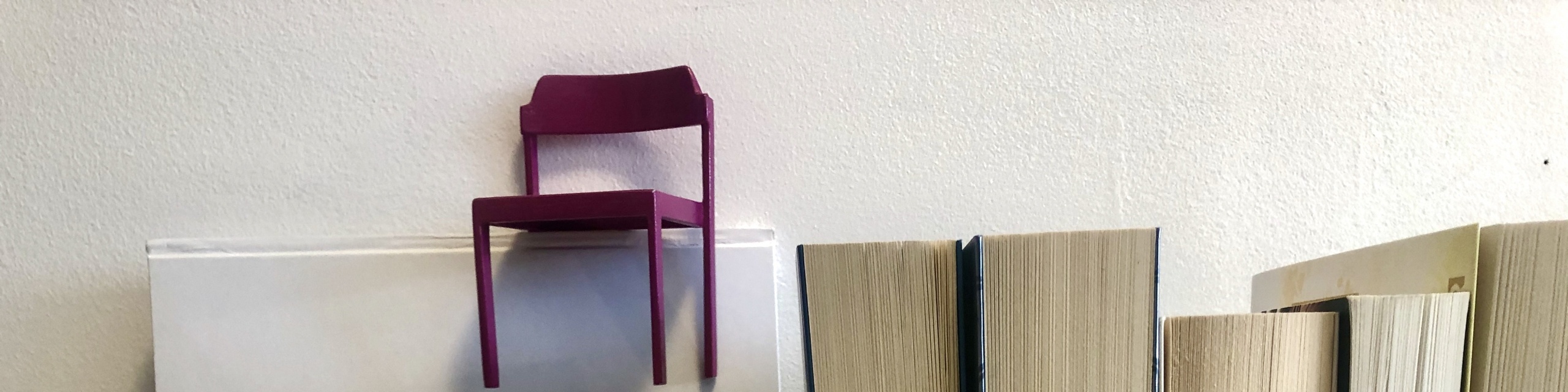 Der pinke Stuhl steht auf hochkant stehenden Büchern.